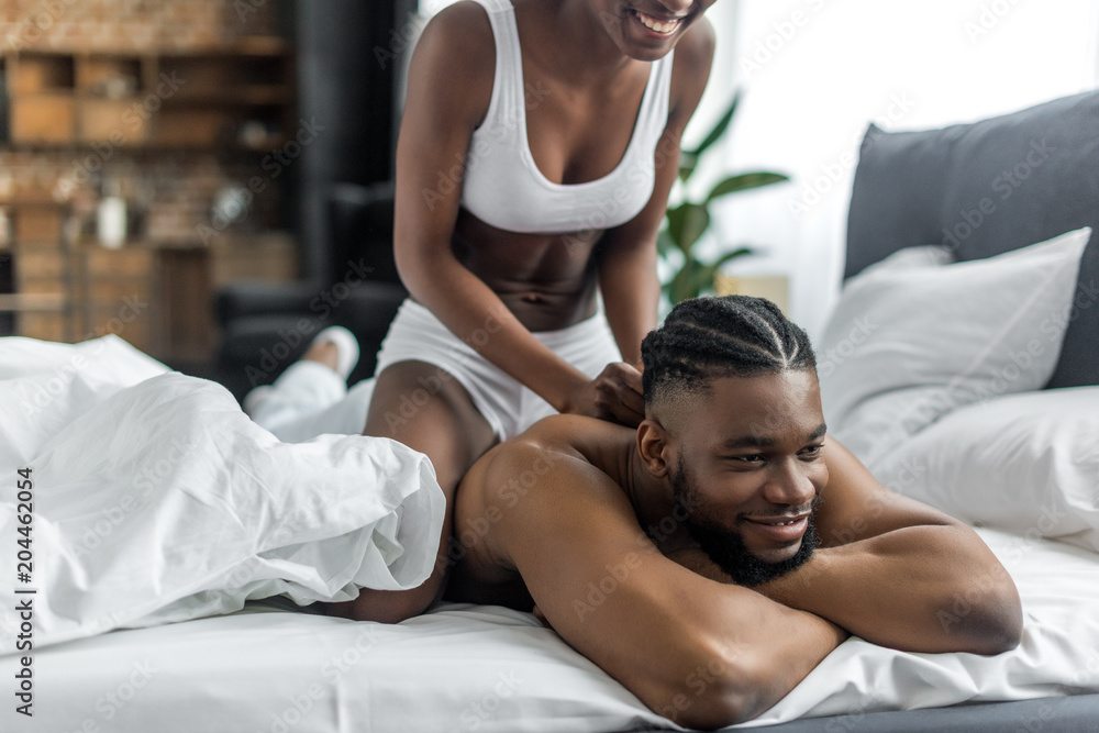 cropped image of african american girlfriend doing massage for boyfriend in bedroom cropped image of african american girlfriend doing massage for boyfriend in bedroom