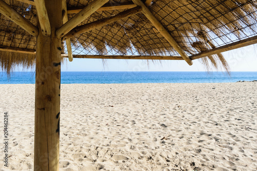 Fototapeta Naklejka Na Ścianę i Meble -  Straw Beach Umbrellas on Sand Beach blue Sea Blue Sky Background. Bright Sunlight. Summer Vacation Wanderlust Traveling Concept. Copy Space