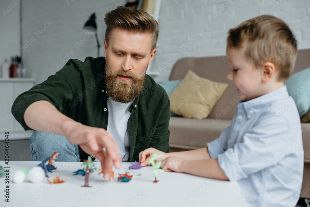 father and cute little son playing with various toy dinosaurs together at home father and cute little son playing with various toy dinosaurs together at home