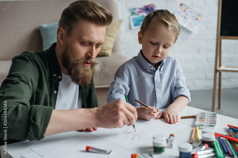 father and cute little son with colorful pencils drawing pictures together at home father and cute little son with colorful pencils drawing pictures together at home
