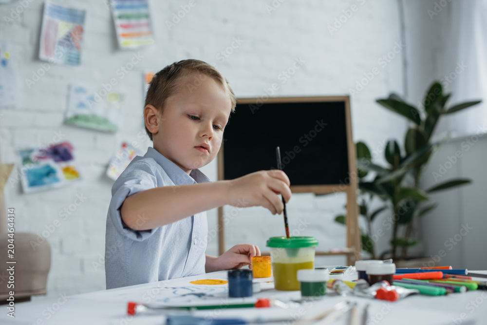 focused little boy with brush and paintings drawing picture alone at home focused little boy with brush and paintings drawing picture alone at home