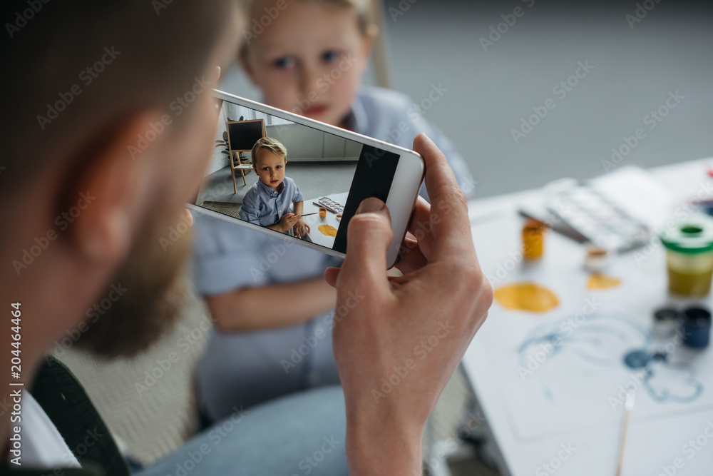 partial view of man taking photo of sons picture on smartphone at home