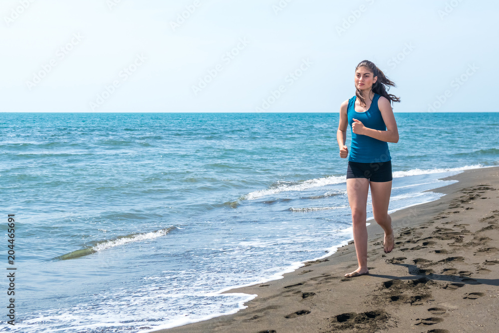 Beautiful sportive girl running along beautiful sandy beach, healthy lifestyle