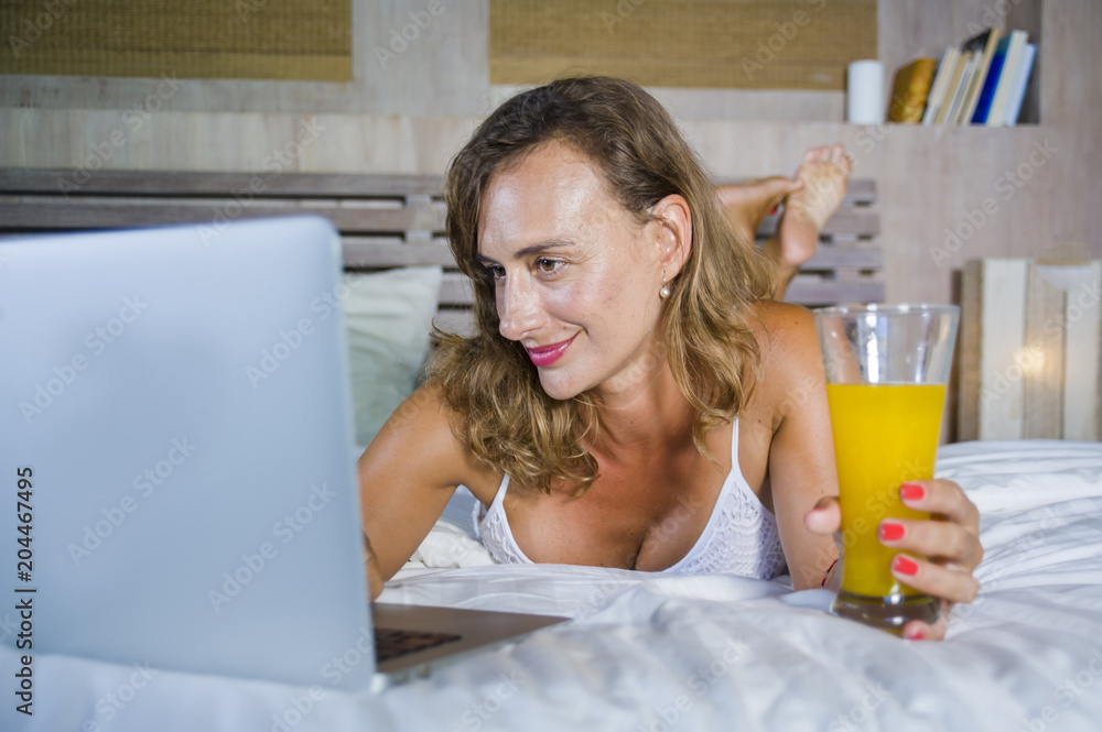 young attractive beautiful happy woman 30s in bed at home using internet working on computer laptop smiling relaxed drinking orange juice young attractive beautiful happy woman 30s in bed at home using internet working on computer laptop smiling relaxed drinking orange juice
