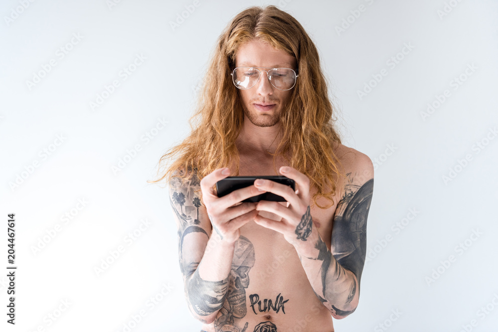 handsome shirtless tattooed man with curly hair using smartphone isolated on white
