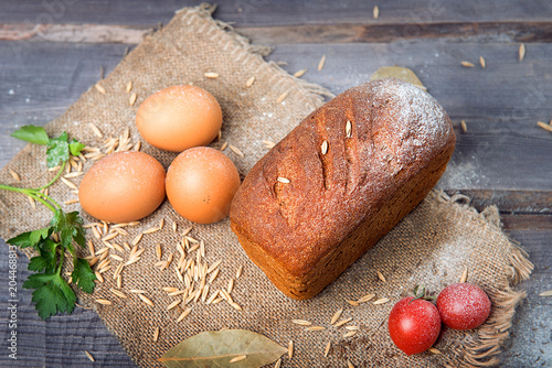 A loaf of rye bread on a wooden table among tomatoes, flour, parsley and chicken eggs. Advertising still life from baking. photo