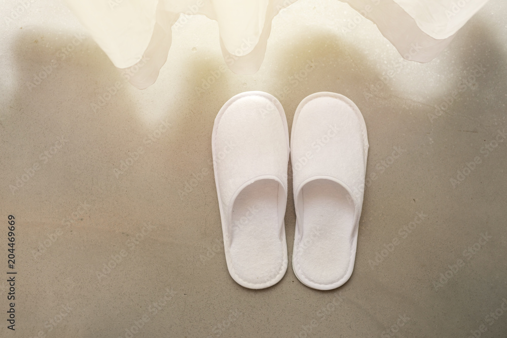White slippers by white sheer curtains and soft sunlight, vacation concept White slippers by white sheer curtains and soft sunlight, vacation concept