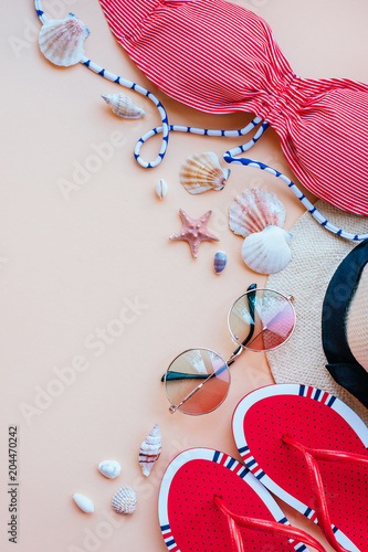 Summer fashion flatlay with gradient round sunglasses, straw hat, flats and red striped bikini top. Decorated with sea shells. Perfect beach set for holidays on the sea. Marina style.