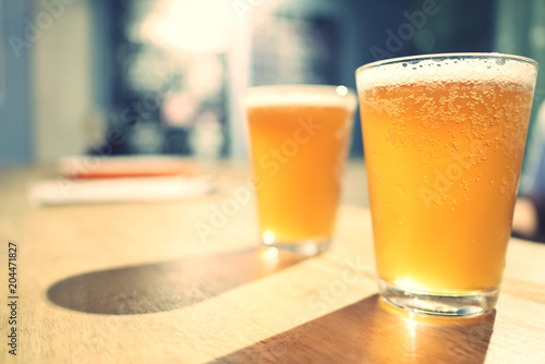 two glasses of cold craft beer with white bubbles and shadow on wooden table at bar