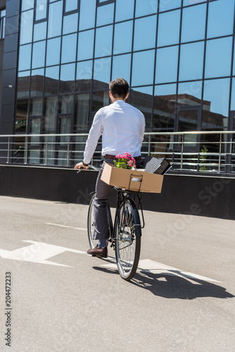 rear view of manager riding on bicycle with box on trunk