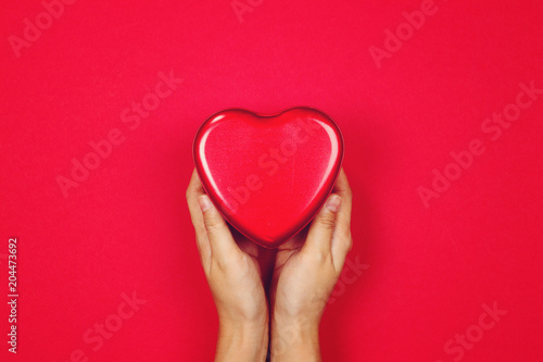 Woman holding red heart in hand on red background with copy space. Flat lay. Top view. Charity Concept.