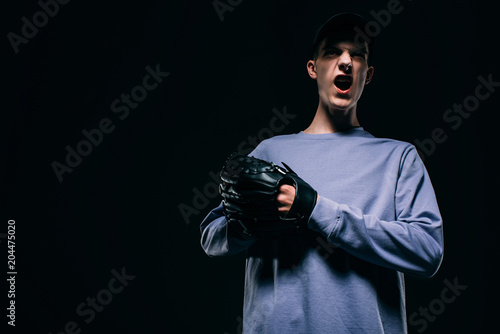 Screaming young man with baseball glove isolated on black