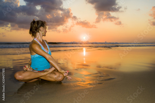young fit and healthy attractive woman practicing fitness and yoga in beautiful sunset beach in meditation and relaxation concept