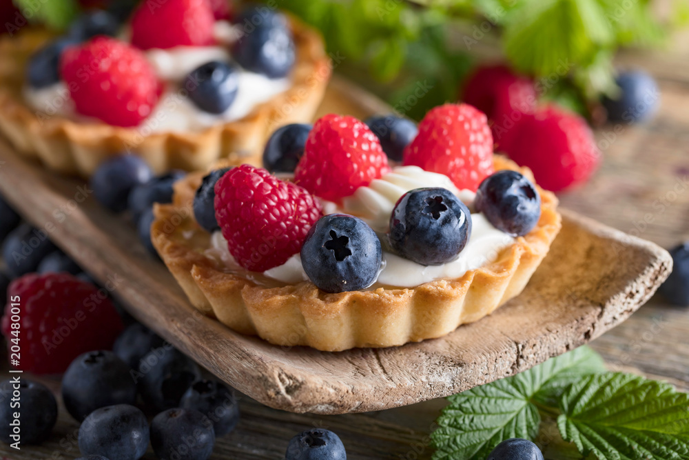 Dessert tarts with raspberries and blueberries on a wooden table. Dessert tarts with raspberries and blueberries on a wooden table.