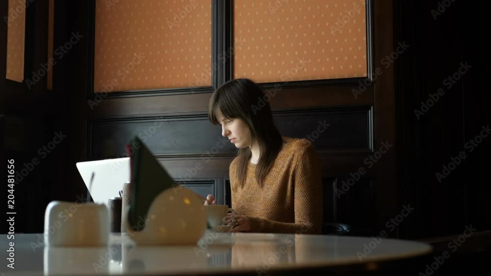 Cute Girl in the Cafe Sitting at the Table Talking on the Phone and Drinking Coffee. The middle plan. In room. Cute Girl in the Cafe Sitting at the Table Talking on the Phone and Drinking Coffee. The middle plan. In room.