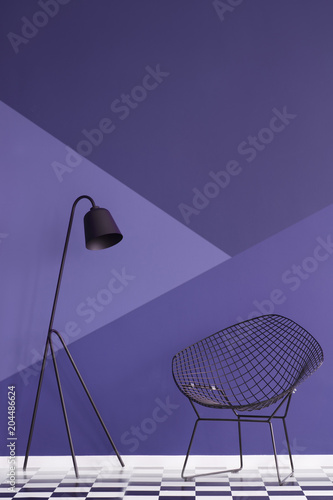 Asymmetrical violet wall in modern living room interior with metal lamp and black armchair on checkered floor. Real photo
