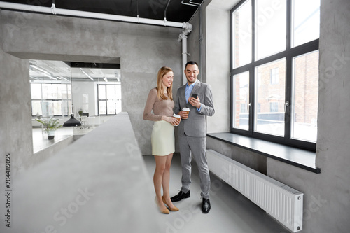 business, technology and corporate concept - happy smiling businesswoman and businessman with smartphone drinking coffee at office