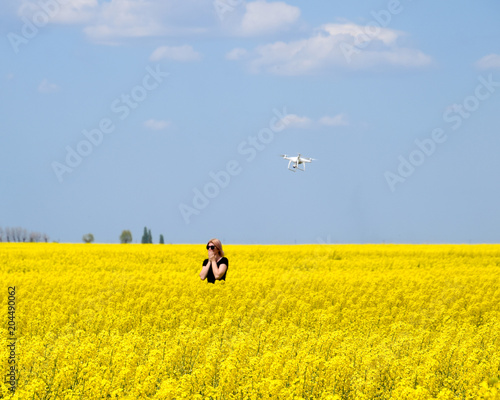 Dron flies after the girl. Shooting with a drone in the field. A girl in a black dress in a field of flowering rape