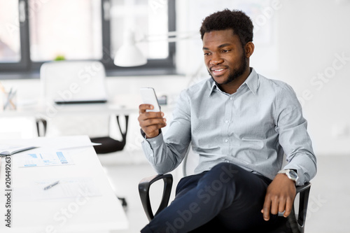 business, people and technology concept - african american businessman with smartphone at office
