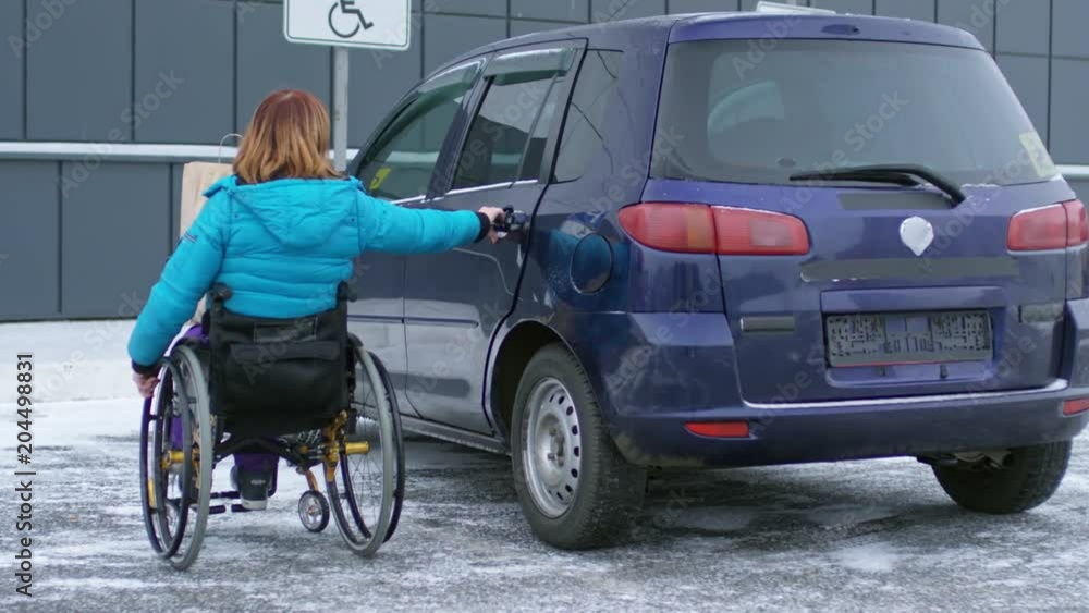 Disabled woman on wheelchair putting bag with groceries on backseat of her car at parking lot Disabled woman on wheelchair putting bag with groceries on backseat of her car at parking lot