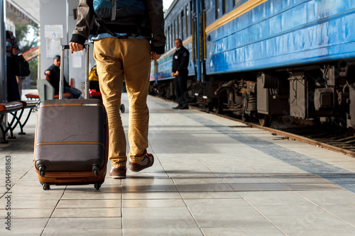 Travel concept. Men wear sneakers shoes and yellow pants travel with brown luggage and backpack on the train station. Sunny day.