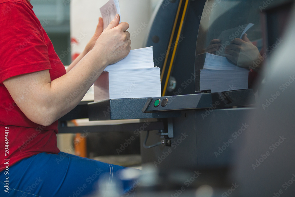 Stack of paper in hands of female worker in front of printing press machine