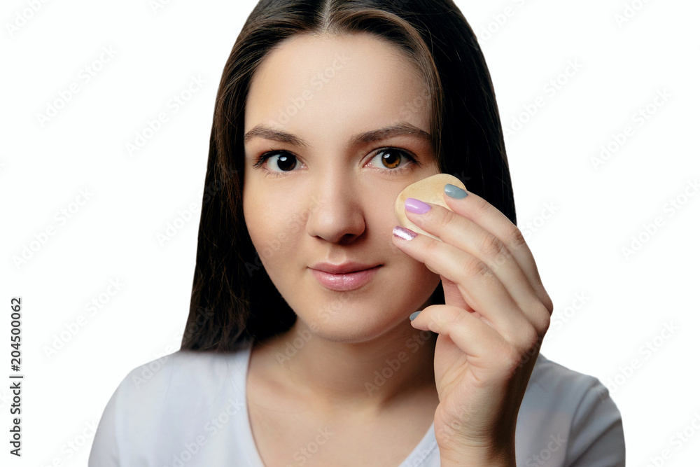 girl puts a foundation on her face with sponge looks at camera girl puts a foundation on her face with sponge looks at camera
