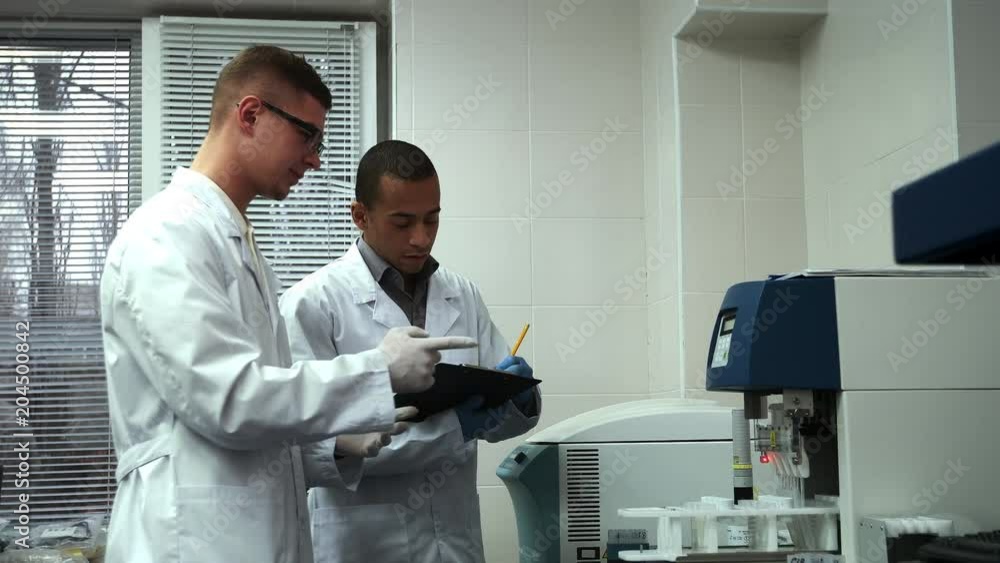 Two male scientists working on laboratory test machine together Two male scientists working on laboratory test machine together