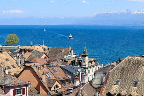 Amazing view over the roofs of old Nyon town at blue Geneva lake or Lac Leman with sailboats and ship and mountains with snow tops at background, Switzerland, Europe photo