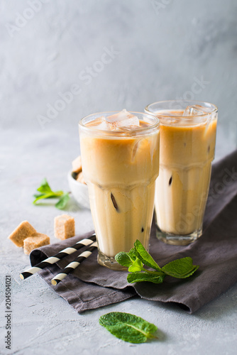 Iced coffee in tall glasses with cream and pieces of sugar, mint and straw