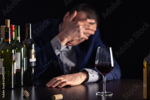 Alcohol abuse by businessman in suit. Silhouette drunk man with glass of wine on first plan.