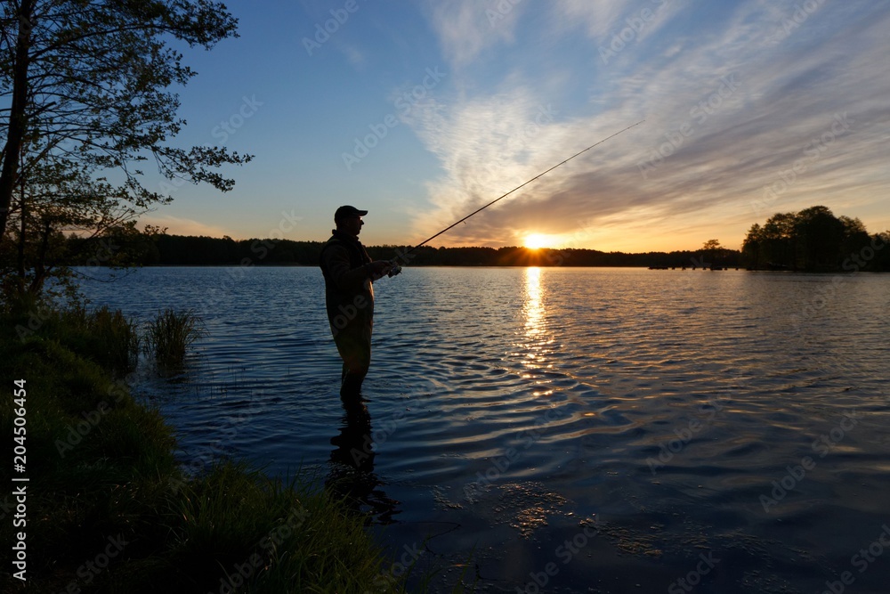 Silhouette of fisherman standing in the lake and catching the fish during sunrise