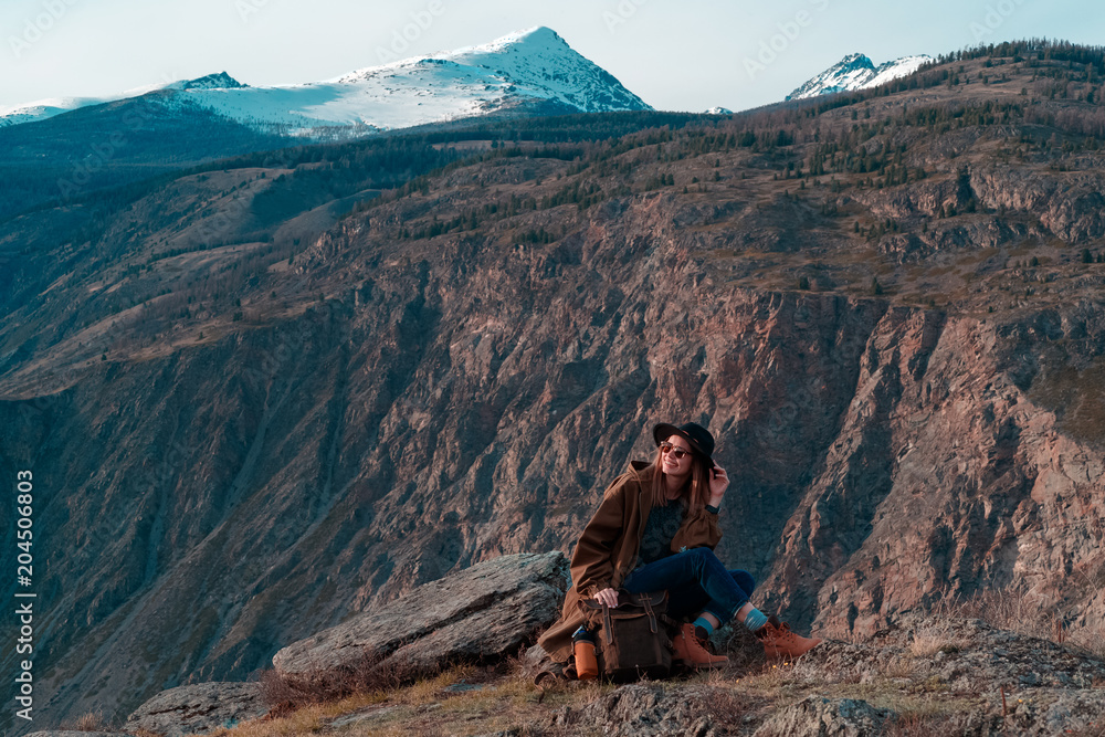 Fototapeta premium Beautiful young woman with retro backpack on the top of cliff amazing mountain range landscape. Sunset. Hipster. Adventure. Travel lifestyle. Copy space.