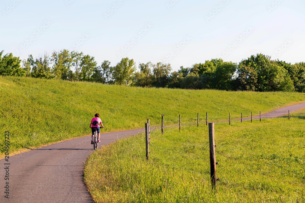 Obraz premium A cyclist rides along the dike in the sunlight
