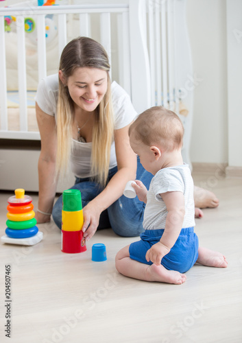 Beautiful young woman sitting with her 10 months old son and playing with toys