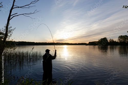 Silhouette of fisherman standing in the lake and catching the fish during sunrise