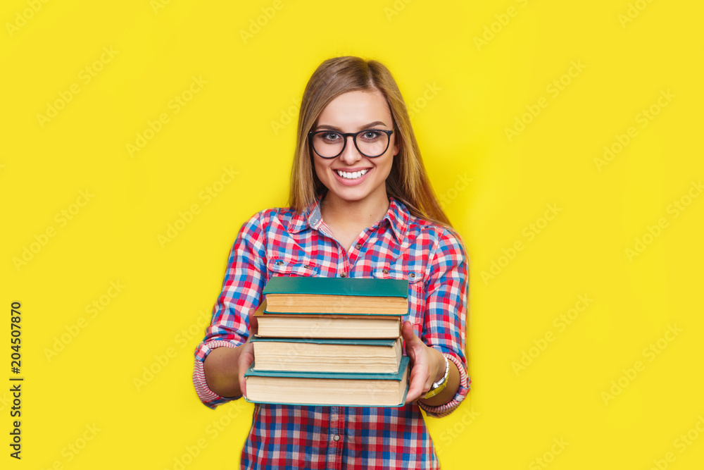 Smiling young stylish student is standing with books on yellow background in glasses and casual bright outfit Smiling young stylish student is standing with books on yellow background in glasses and casual bright outfit