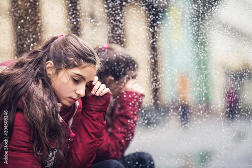 sad girl sits on street near wet mirror in autumn afternoon.