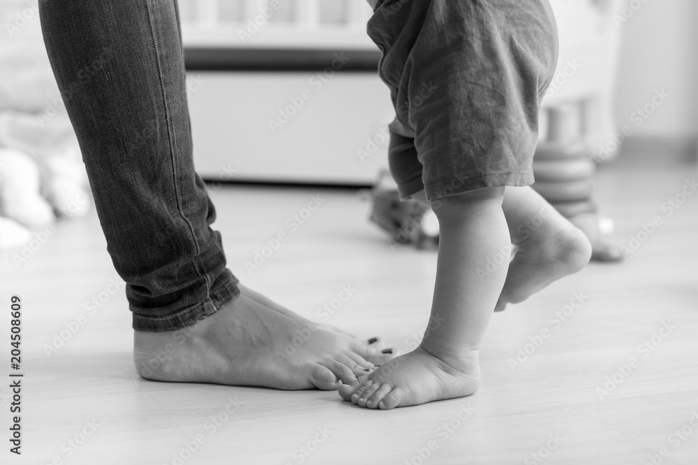 Closeup black and white image of baby's feet next to mother's on wooden floor at house