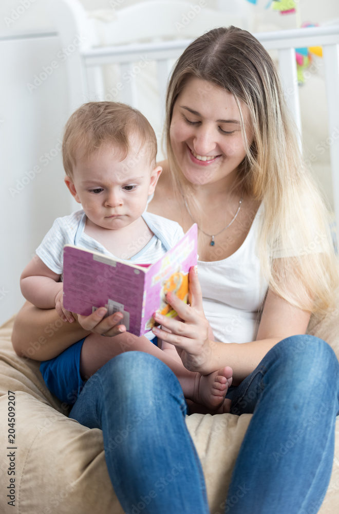 Portrait of smiling young mother sitting on beanbag with her baby boy and reading him book Portrait of smiling young mother sitting on beanbag with her baby boy and reading him book