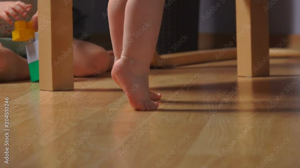 barefoot toddler on tiptoe near an armchair with kid playing on the background barefoot toddler on tiptoe near an armchair with kid playing on the background