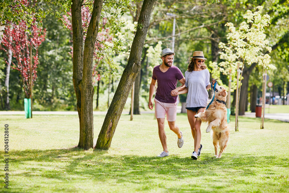 Fototapeta premium Young couple running and playing with their dog outdoors in the morning