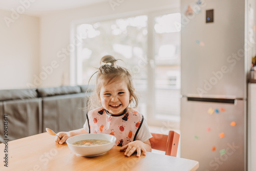 adorable funny toddler girl eating soup at the modern open kitchen