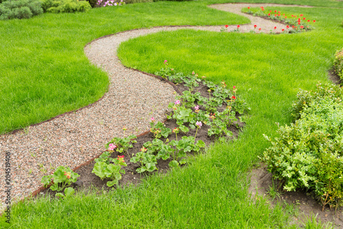 a winding footpath in the garden, a path of small gravel, green grass and flowers along the path