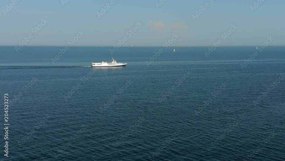 Big white yacht sailing far out in a sea leaving water trails under sunlight on deep blue sea water background. Ships, boats and vessels on a horizon. Sunny summer day, clear blue sky. Wind and waves. Big white yacht sailing far out in a sea leaving water trails under sunlight on deep blue sea water background. Ships, boats and vessels on a horizon. Sunny summer day, clear blue sky. Wind and waves.