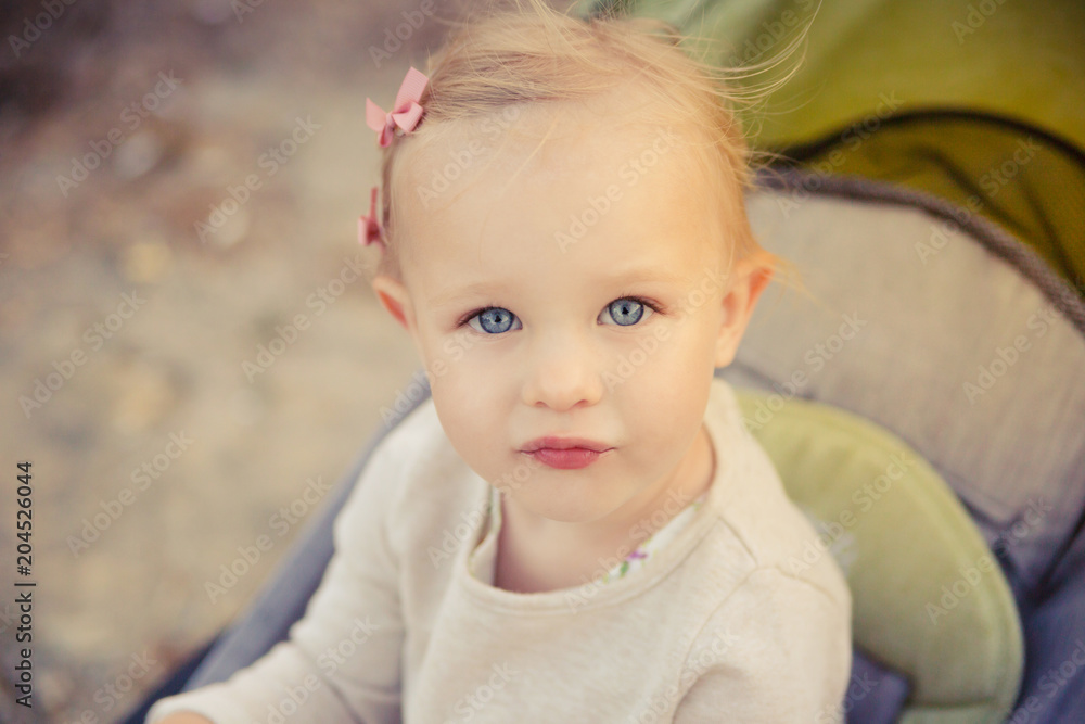 Cute sad blonde baby girl with blue eyes in a stroller. Cute sad blonde baby girl with blue eyes in a stroller.
