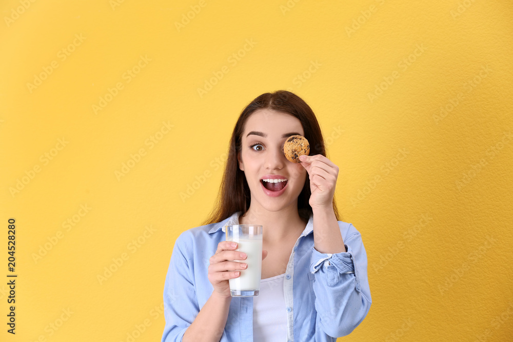 Beautiful young woman drinking milk with cookie on color background Beautiful young woman drinking milk with cookie on color background
