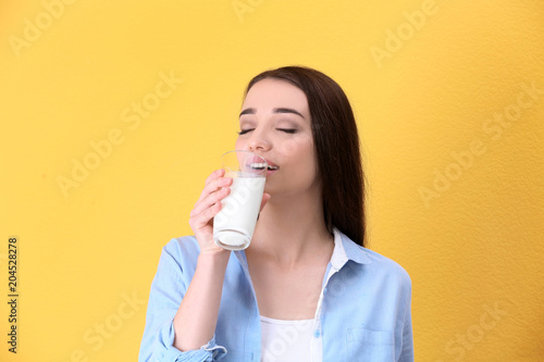 Beautiful young woman drinking milk on color background