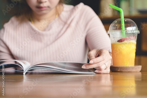 Asian woman smile and reading magazine book and drink orange juice smoothie in cafe.