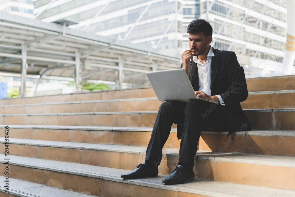 Handsome young manager working on laptop while sitting outdoors on the stairs, concept of thinking analysis and big data. Handsome young manager working on laptop while sitting outdoors on the stairs, concept of thinking analysis and big data.